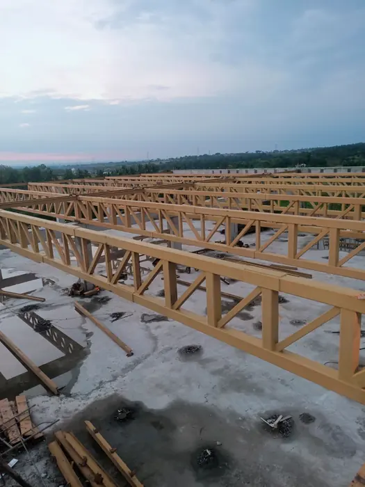 Series of fabricated roof trusses assembled across a large project floor.