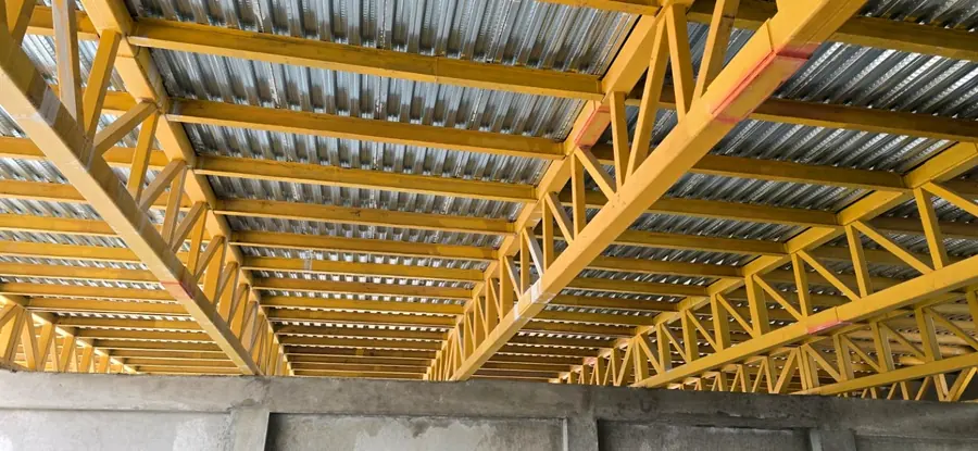 Yellow steel trusses and galvanized deck sheets installed over a structural floor.