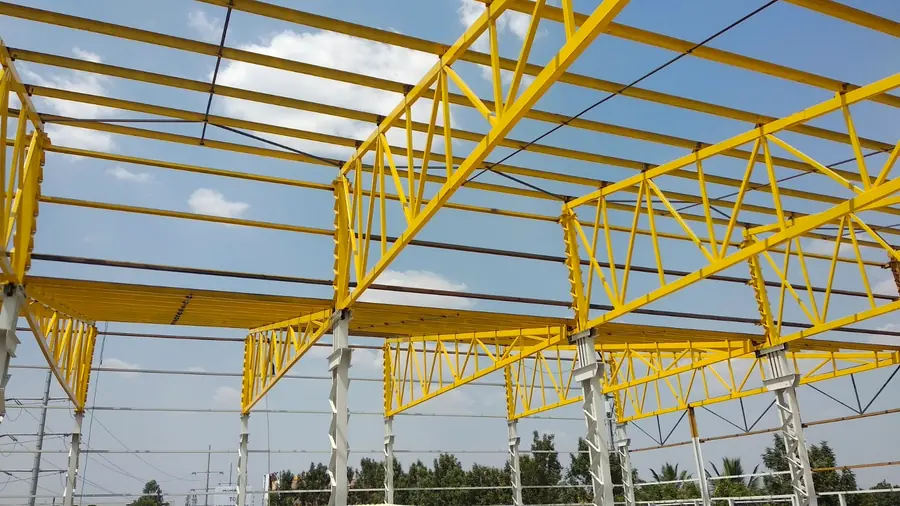 Yellow industrial roof frame with long steel trusses and purlins.